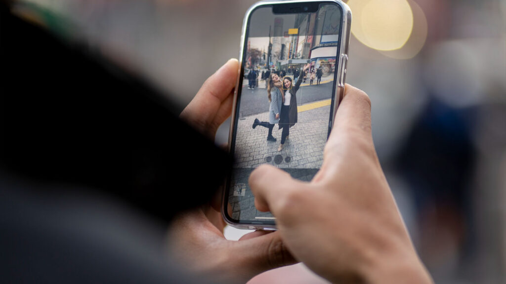Eine Person macht mit einem Smartphone ein Foto von zwei Menschen, die verspielt auf einer Stadtstraße posieren, und hält den Moment mühelos fest, als würde sie nahtlos durch eine gut gestaltete Website navigieren.
